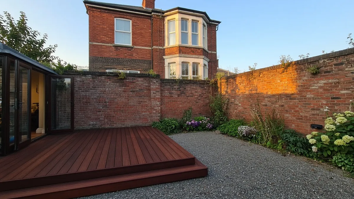 Example image: oiled dark hardwood deck sheltered by a high brick wall behind a Victorian house